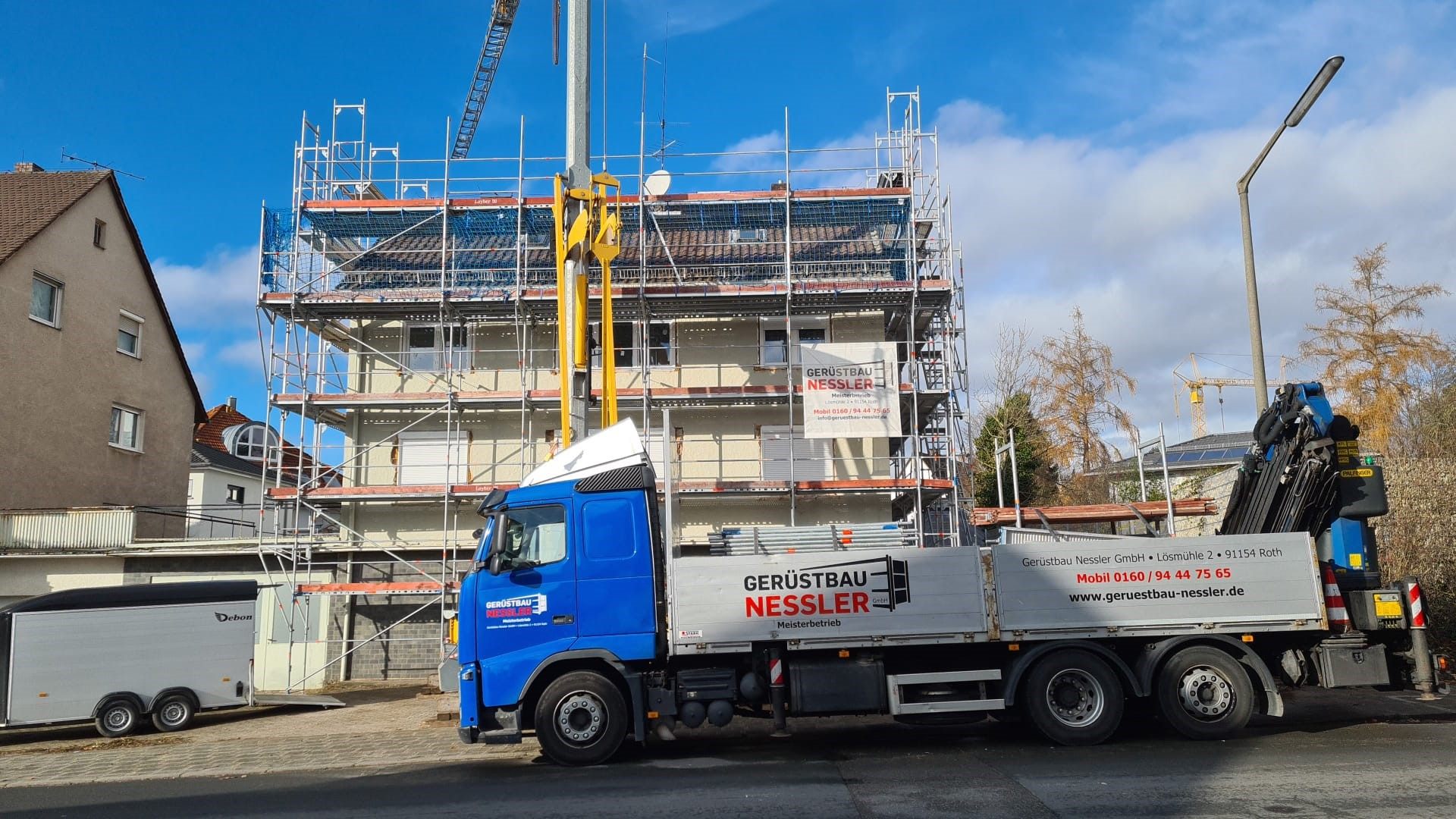 Nessler-LKW mit Kran vor einem eingerüsteten Wohnhaus